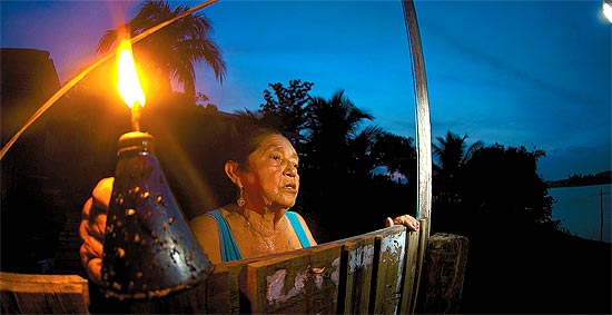 Maria Assunção, 74, com a lamparina que usa à noite em sua casa, às margens do lago da maior hidrelétrica 100% em território nacional, Tucuruí (PA)