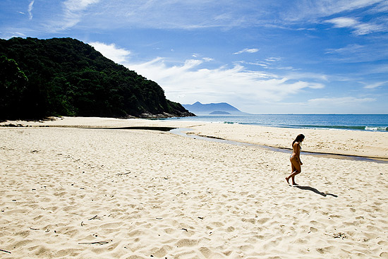 Mulher caminha na praia Brava de Boiçucanga, em São Sebastião, no litoral norte de São Paulo